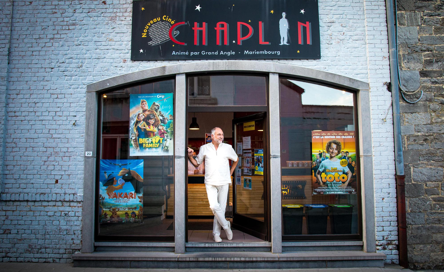 Man voor de deuropening van Ciné Chaplin, witte gevel met filmposters.