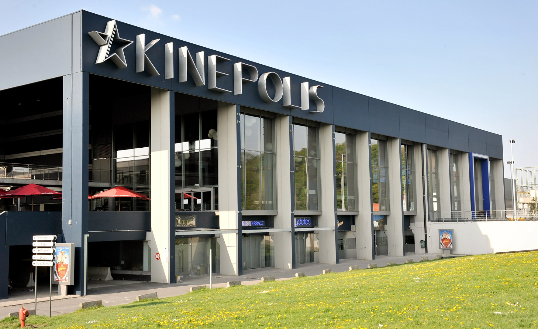 Gevel van bioscoop Kinepolis Kortrijk met terras en gazon.