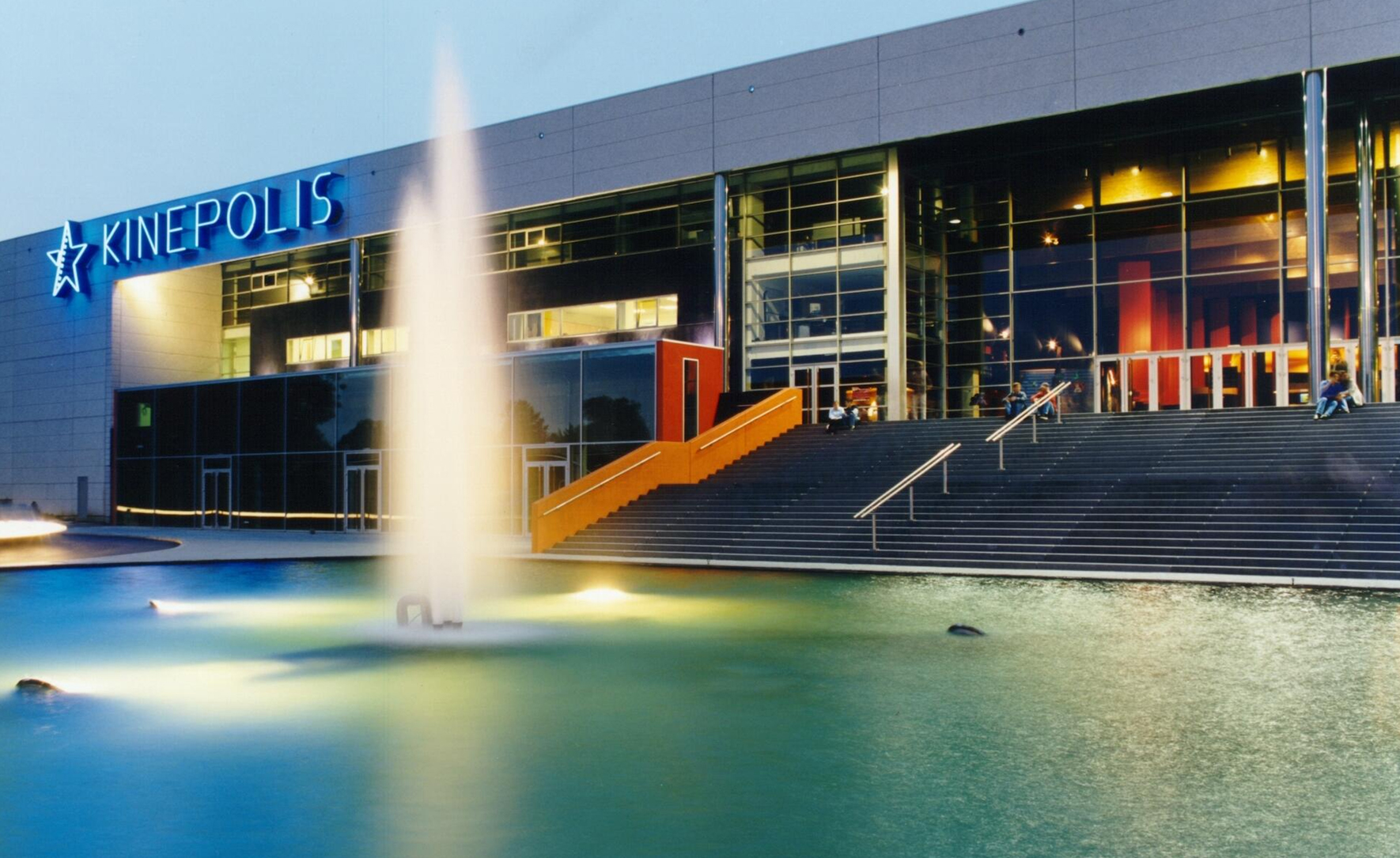 Bioscoop Kinepolis met verlichte fontein bij avond.